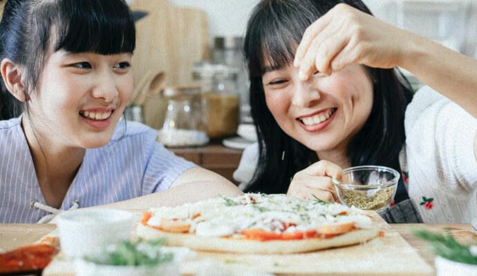 Two people are seasoning a meal together and smiling