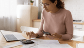 A woman sits at a desk looking at a calculator.