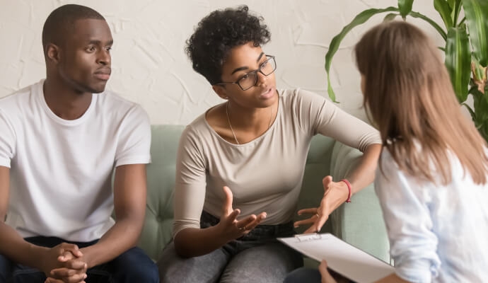 A couple sits next to each other on a couch facing a therapist