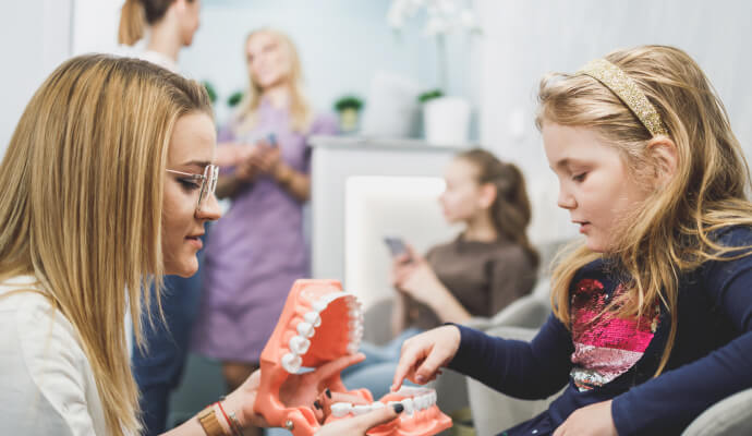 A woman is holding a plastic mouth with teeth. The mouth is open wide, and a young child is pointing to one of the teeth.